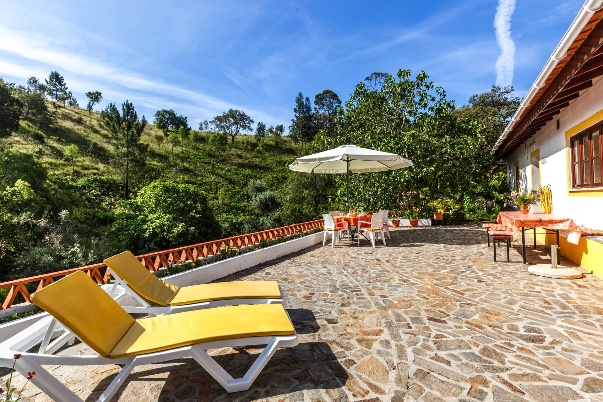 The stone terrace of Casa Amarela, with sun loungers and a view over wooded hills