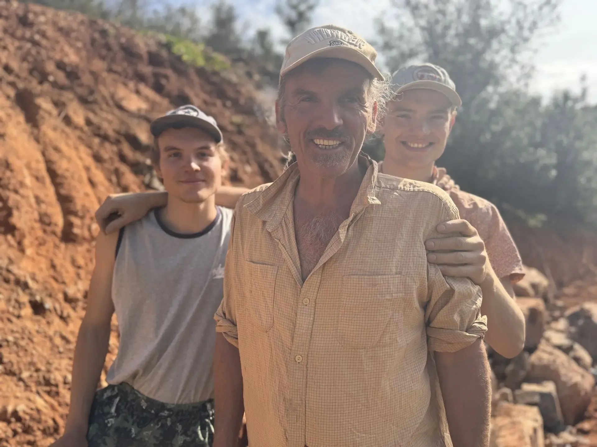 Steven McKay on site with two young builders, red earth cut behind them