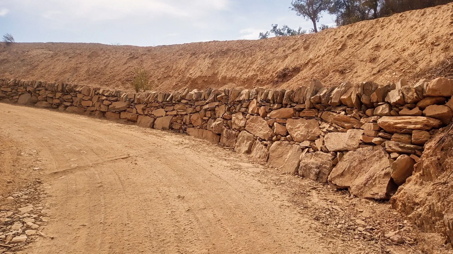 Long dry stone retaining wall holding a cut bank above a farm track